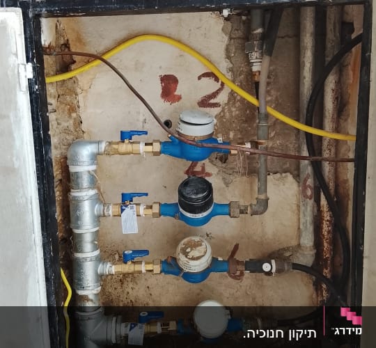 מד מים עם צינורות וחיבורים בקיר